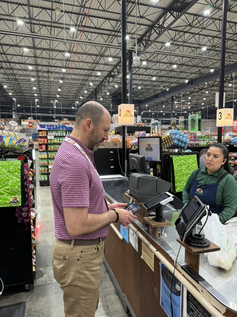 A shopper using a phone at a Nam Dae Mun Market checkout lane with an AppCard In-Lane Terminal